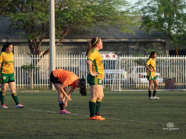Young female soccer players in yellow and green uniforms during a match on grass field with white fence in background