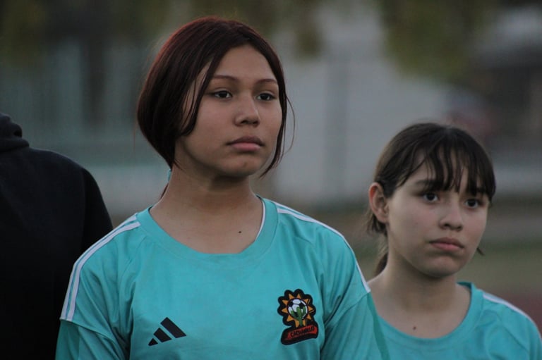 Two young girls in turquoise sports uniforms standing outdoors with a blurred background
