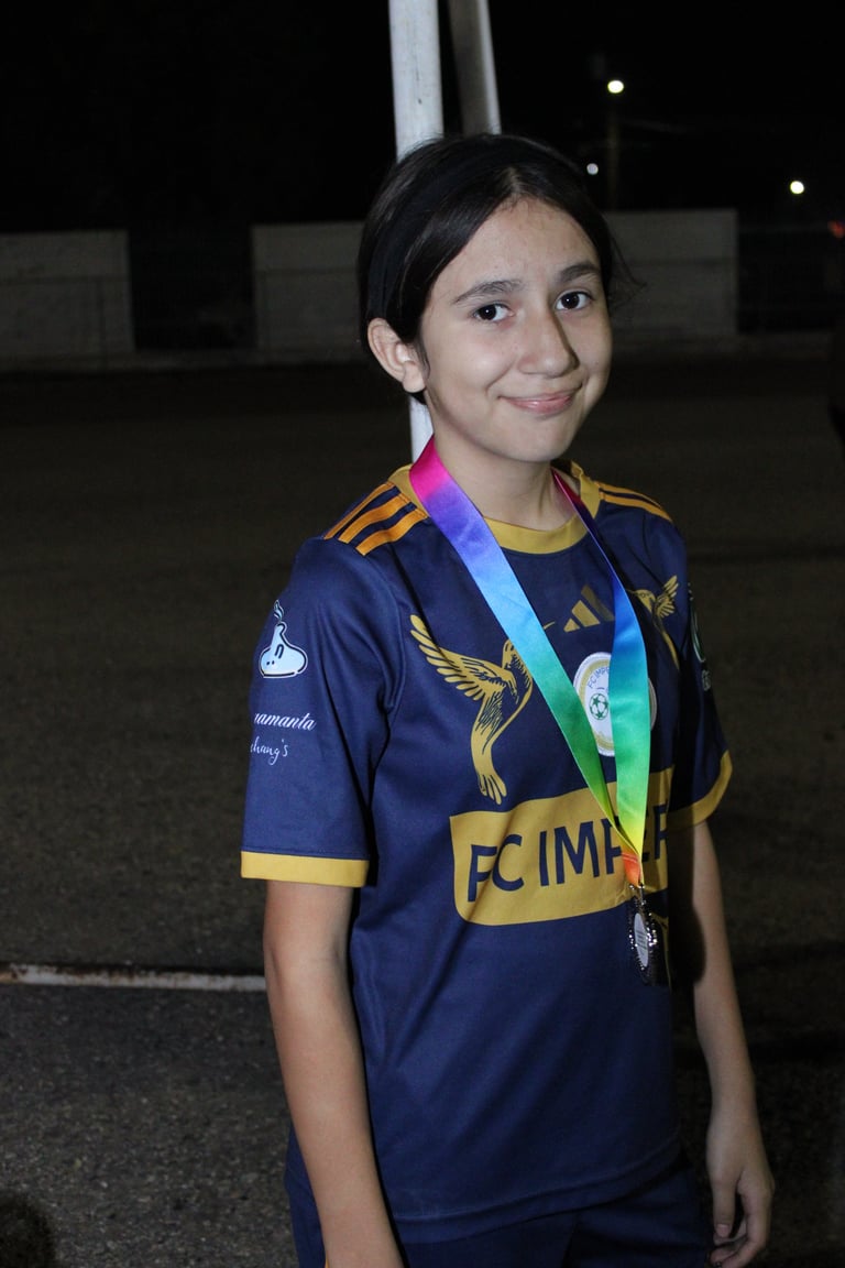 Young girl wearing navy and gold sports jersey with medal around neck, smiling at camera outdoors at night