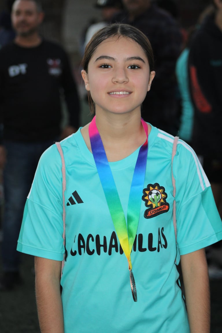 Young girl wearing turquoise sports jersey and rainbow medal, smiling at camera with crowd in background
