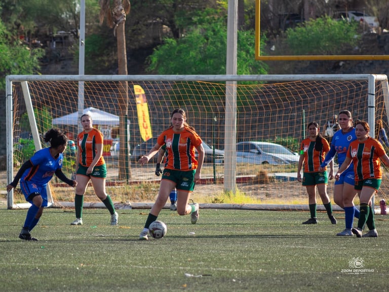 Youth soccer players in orange and blue jerseys competing on a field with a net and goal in background