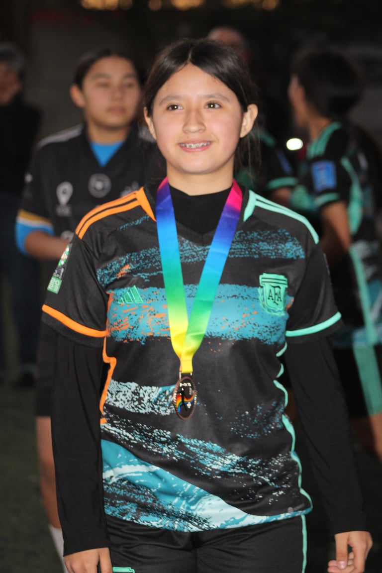 Young girl wearing colorful medal around neck, smiling at camera in black and turquoise athletic jersey